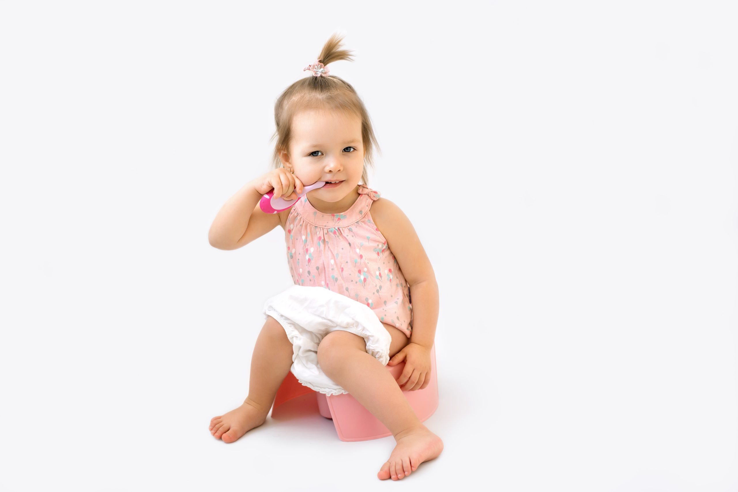 ?ute girl is brushing teeth with a toothbrush while sitting on a potty.